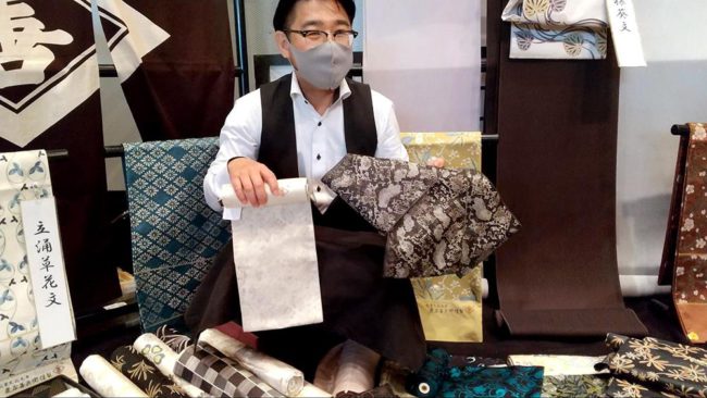 素材に漆が使われている、へび皮の文様が描かれた小袋帯を紹介する専務。